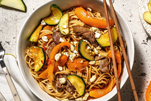 Wok de nouilles sautées au boeuf mariné avec de la courgette, du poivron et des noix de cajou