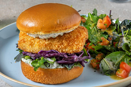 Burger de lieu pané à la mayonnaise aux herbes avec une salade de chou rouge, jeunes pousses et tomate